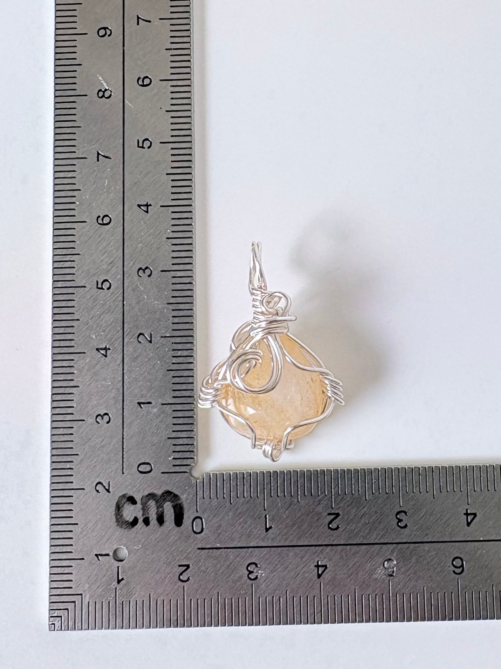 silver wire wrapped citrine pendant next to an "L" shaped ruler for scale all against a white background.
