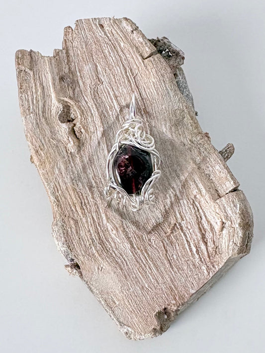 Silver wire-wrapped garnet pendant  on a piece of driftwood against a light background