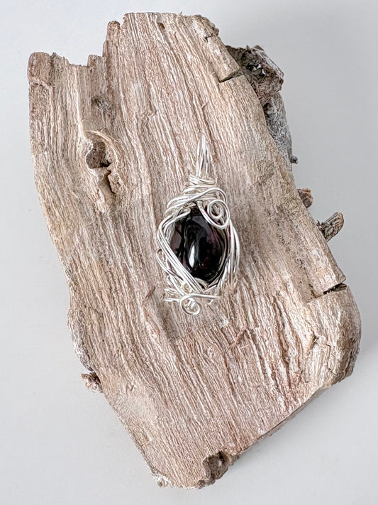 Silver wire-wrapped garnet pendant  on a piece of driftwood against a light background