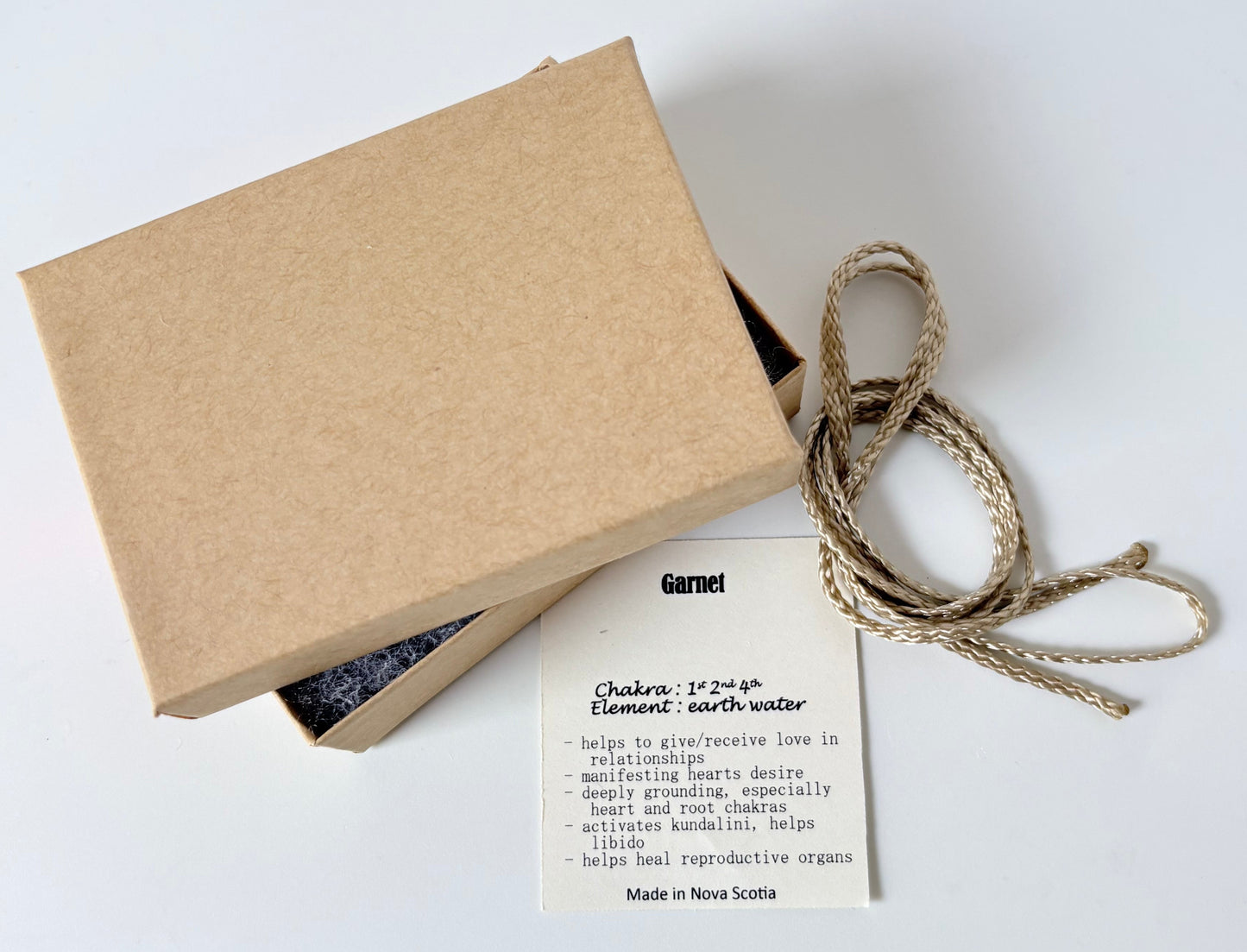 Kraft paper jewelry box with a garnet information tag and cream colour cord for a pendant on a white background