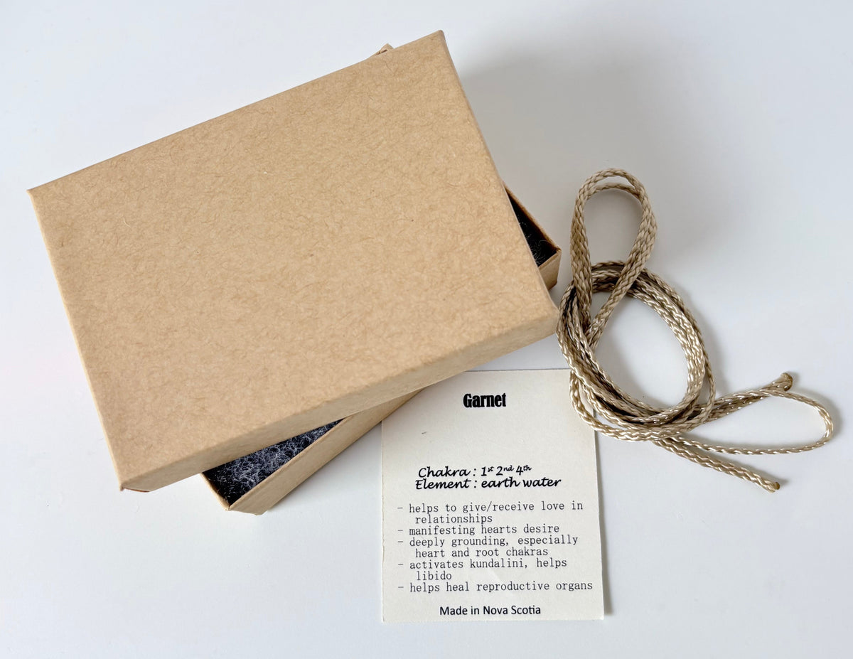 Kraft paper jewelry box with a garnet information tag and cream colour cord for a pendant on a white 