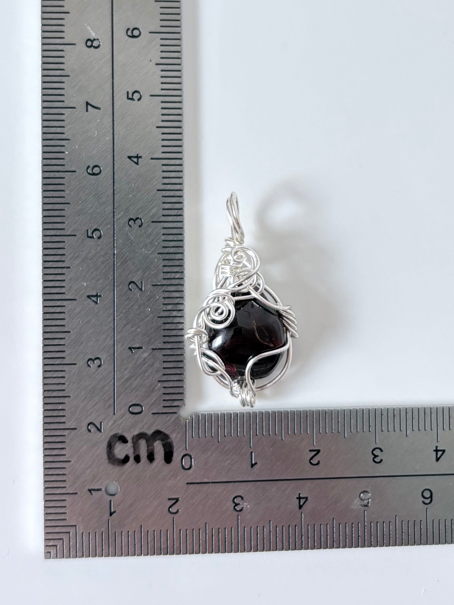 silver wire wrapped garnet pendant next to an "L" shaped ruler for scale all against a white background.