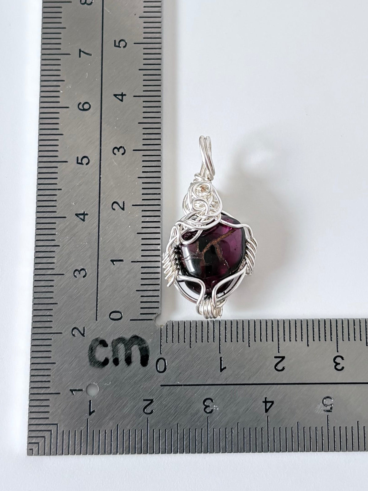 silver wire wrapped garnet pendant next to an "L" shaped ruler for scale all against a white background.