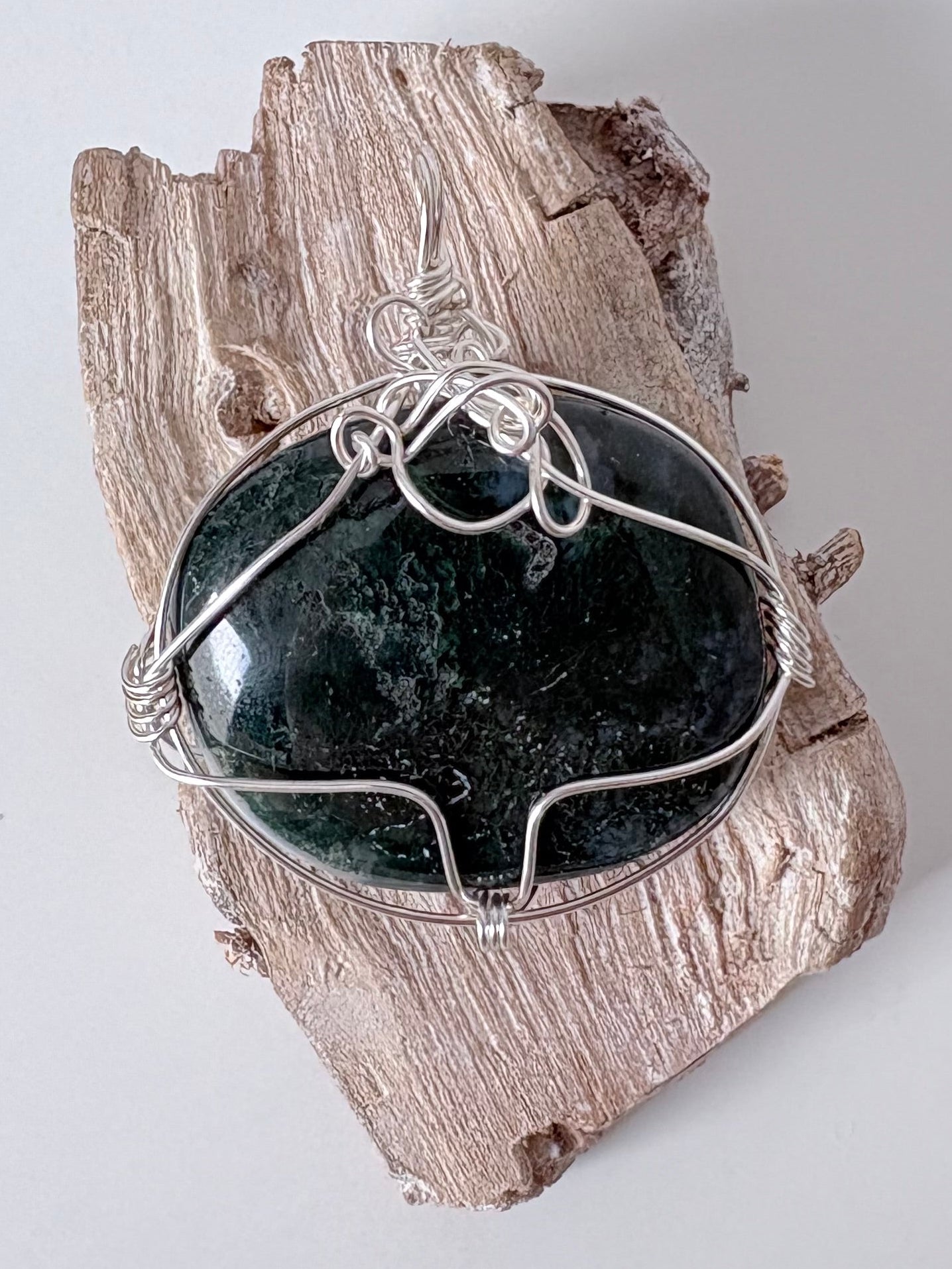 Silver wire-wrapped moss agate pendant  on a piece of driftwood against a light background