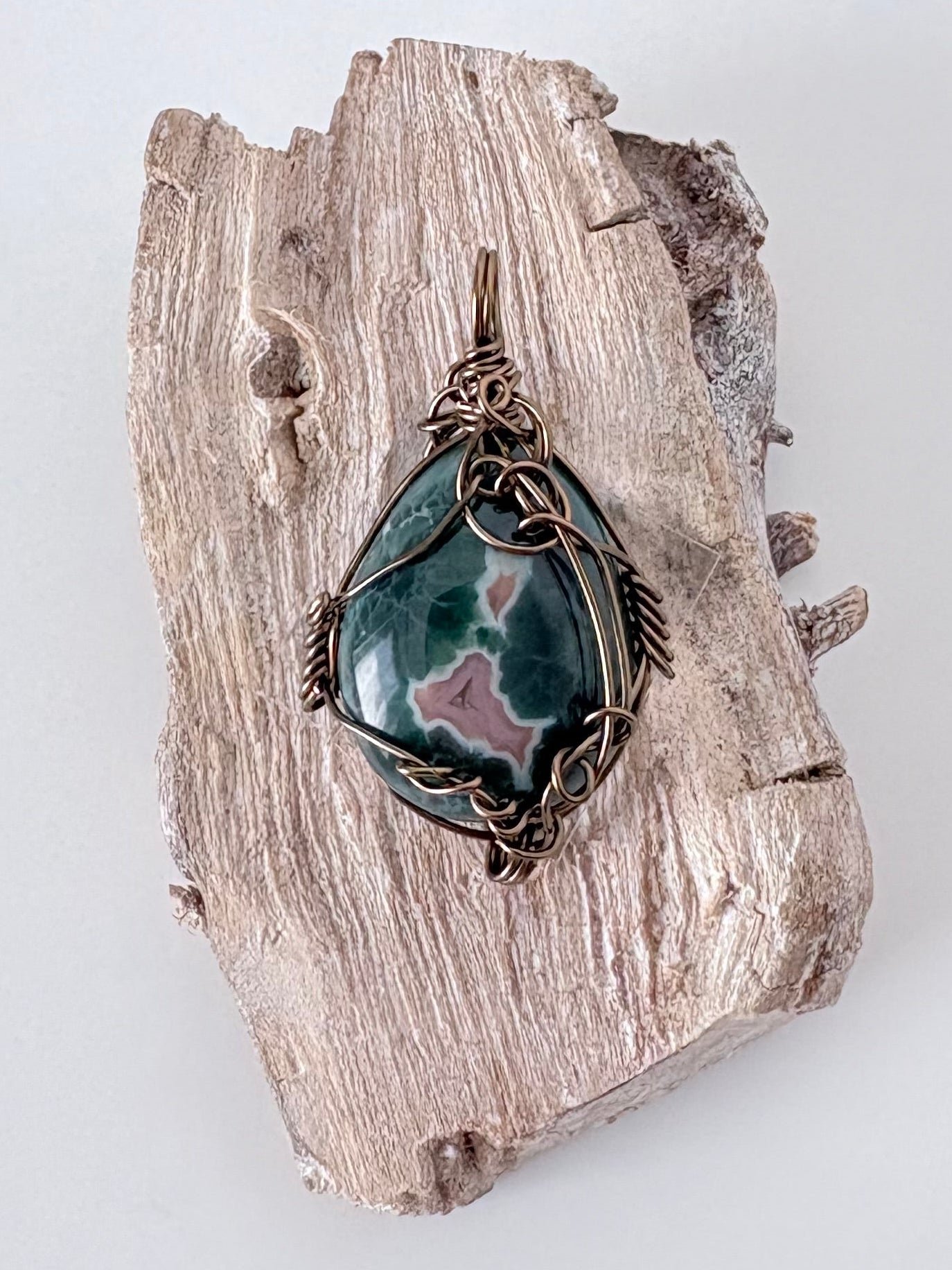 Silver wire-wrapped ocean jasper pendant  on a piece of driftwood against a light background