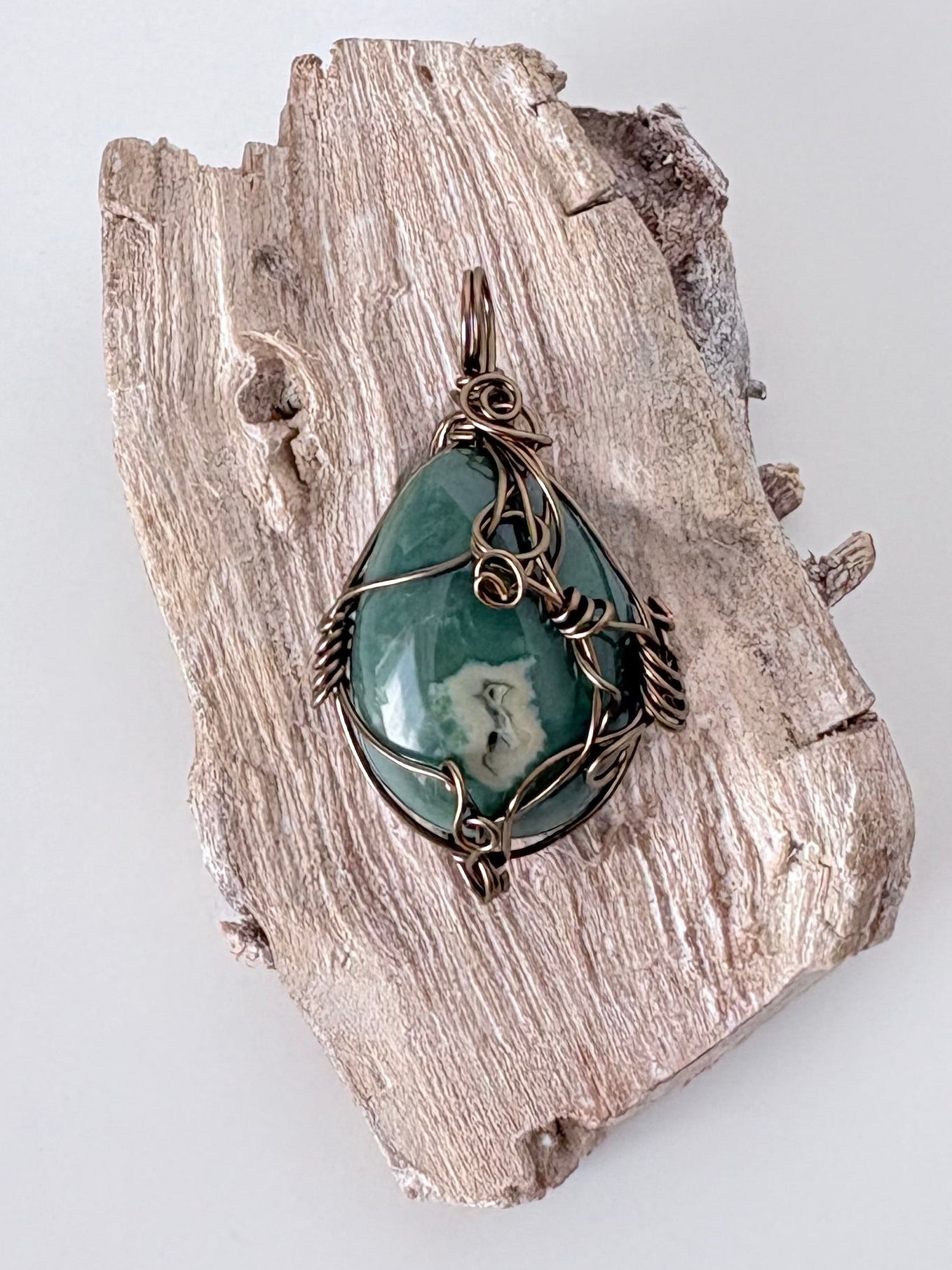 Silver wire-wrapped ocean jasper pendant  on a piece of driftwood against a light background