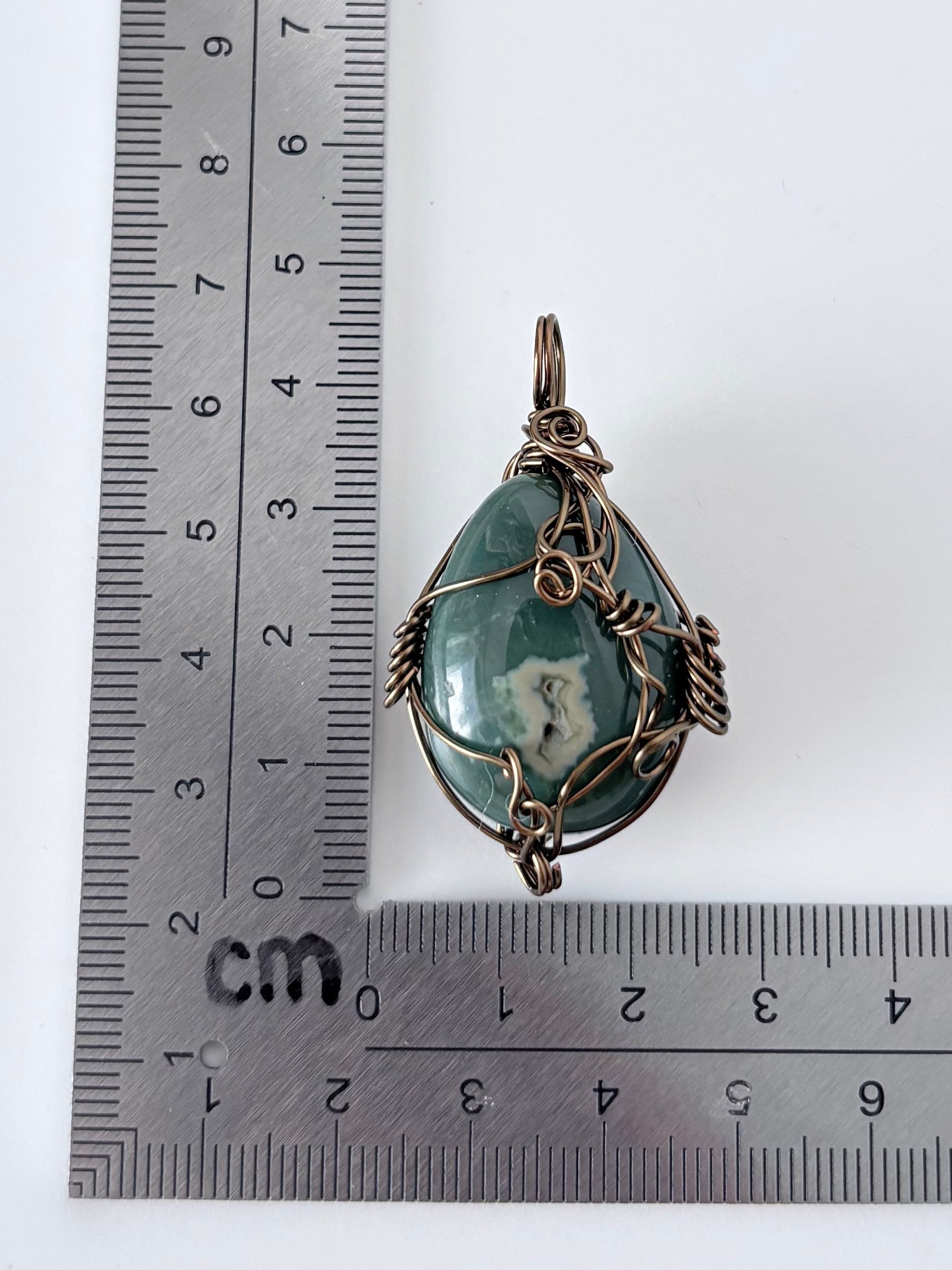 silver wire wrapped ocean jasper pendant next to an "L" shaped ruler for scale all against a white background.