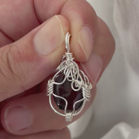 hand holding and moving the silver wire wrapped  garnet pendant around so all the sides of it are shown. done against a white background.