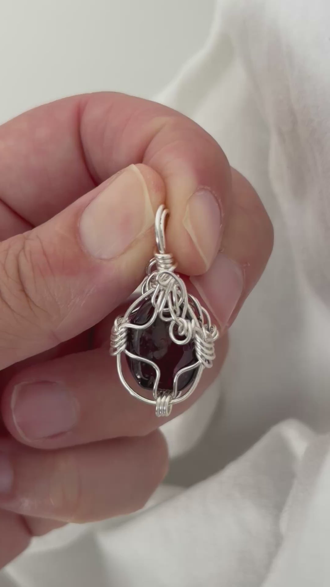 hand holding and moving the silver wire wrapped  garnet pendant around so all the sides of it are shown. done against a white background.