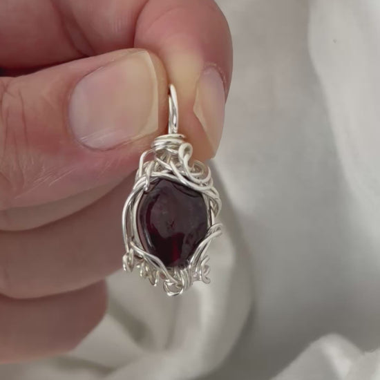hand holding and moving the silver wire wrapped  garnet pendant around so all the sides of it are shown. done against a white background.