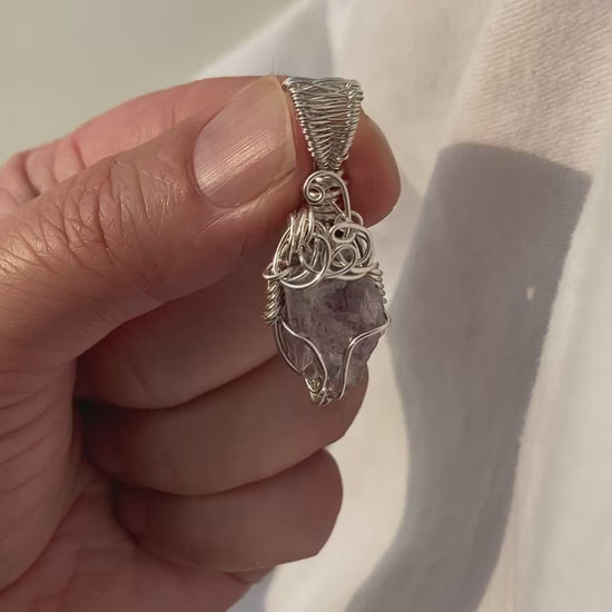 Lepidolite Pendant - Video of a wire-wrapped purple lepidolite stone pendant held between fingers over a white background, showing all sides of the pendant in natural lighting.