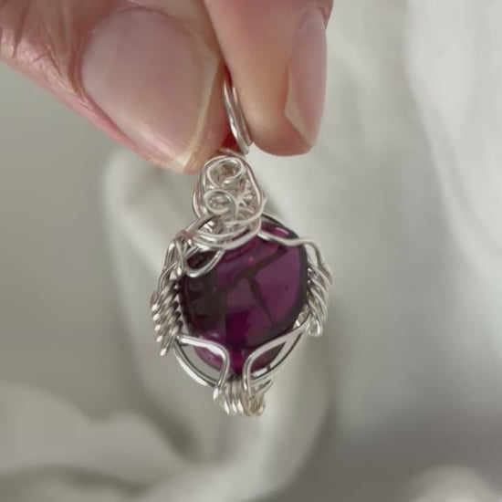 hand holding and moving the silver wire wrapped  garnet pendant around so all the sides of it are shown. done against a white background.
