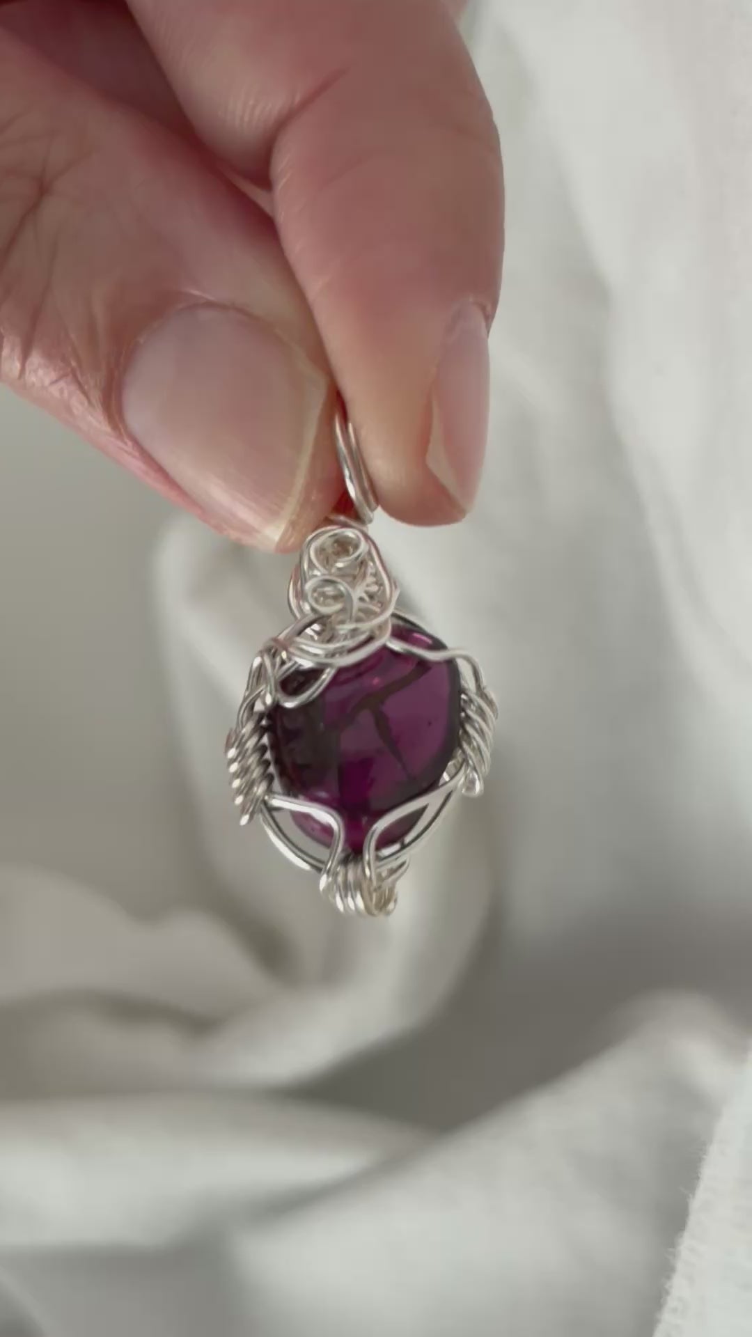 hand holding and moving the silver wire wrapped  garnet pendant around so all the sides of it are shown. done against a white background.
