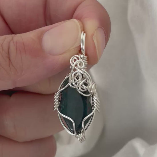 hand holding and moving the silver wire wrapped  bloodstone pendant around so all the sides of it are shown. done against a white background.