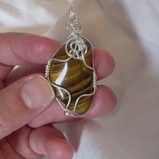 silver wire wrapped tigers eye pendant held by a hand being rotated in a video