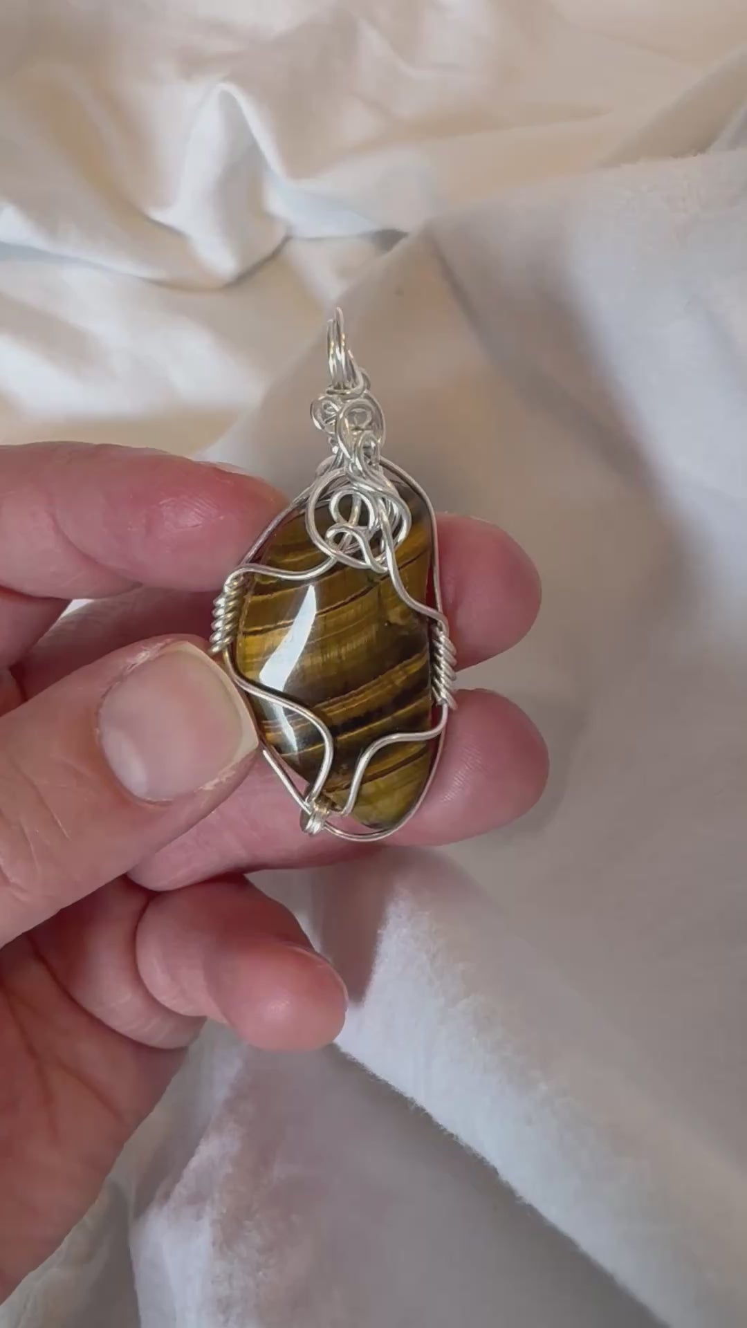 silver wire wrapped tigers eye pendant held by a hand being rotated in a video