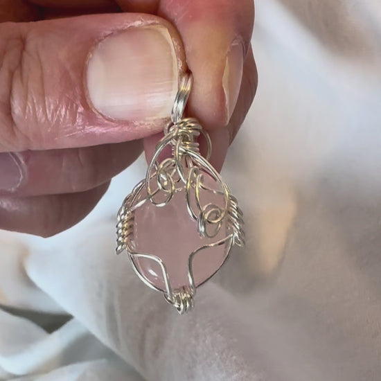Rose quartz pendant, silver wire wrapped, being held by a hand and rotated in a video with a white background.