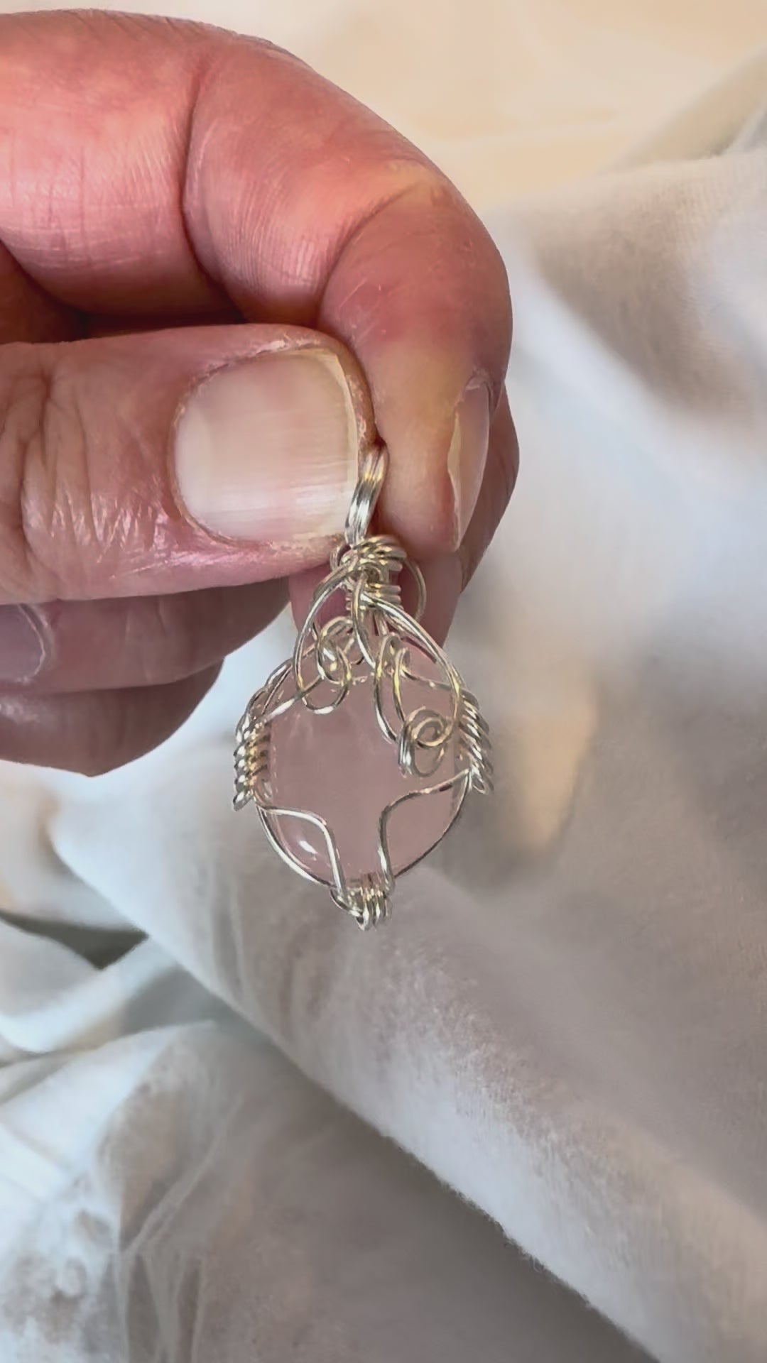 Rose quartz pendant, silver wire wrapped, being held by a hand and rotated in a video with a white background.