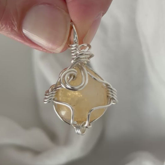 hand holding and moving the silver wire wrapped  citrine pendant around so all the sides of it are shown. done against a white background.