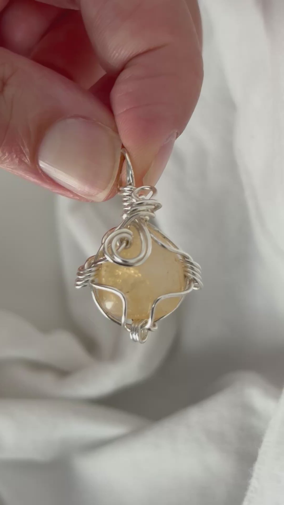 hand holding and moving the silver wire wrapped  citrine pendant around so all the sides of it are shown. done against a white background.