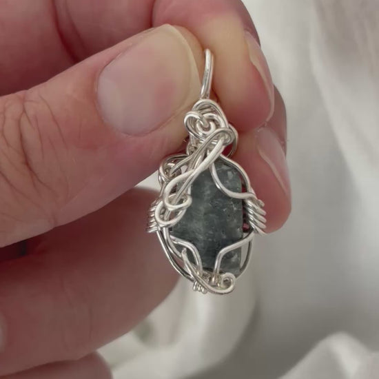 hand holding and moving the silver wire wrapped blue sapphire pendant around so all the sides of it are shown. done against a white background.