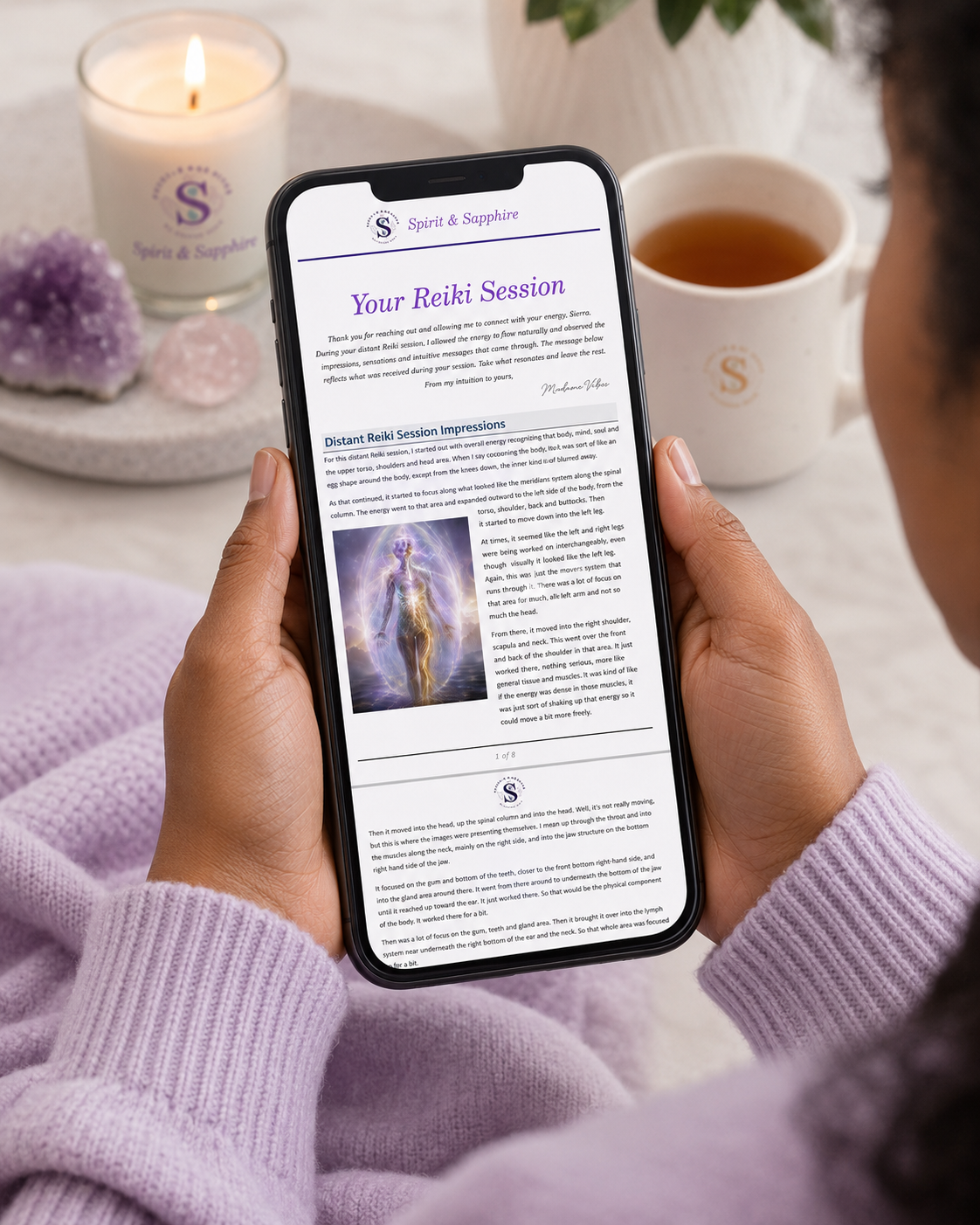 Person holding a phone with a Spirit and Sapphire distant Reiki session write up open, surrounded by a candle, mug, and crystals.